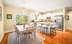 A modern kitchen with white cabinets, stainless steel appliances, and a wooden dining table with chairs.