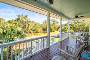 A covered porch with white railings, wooden flooring, and a ceiling fan.