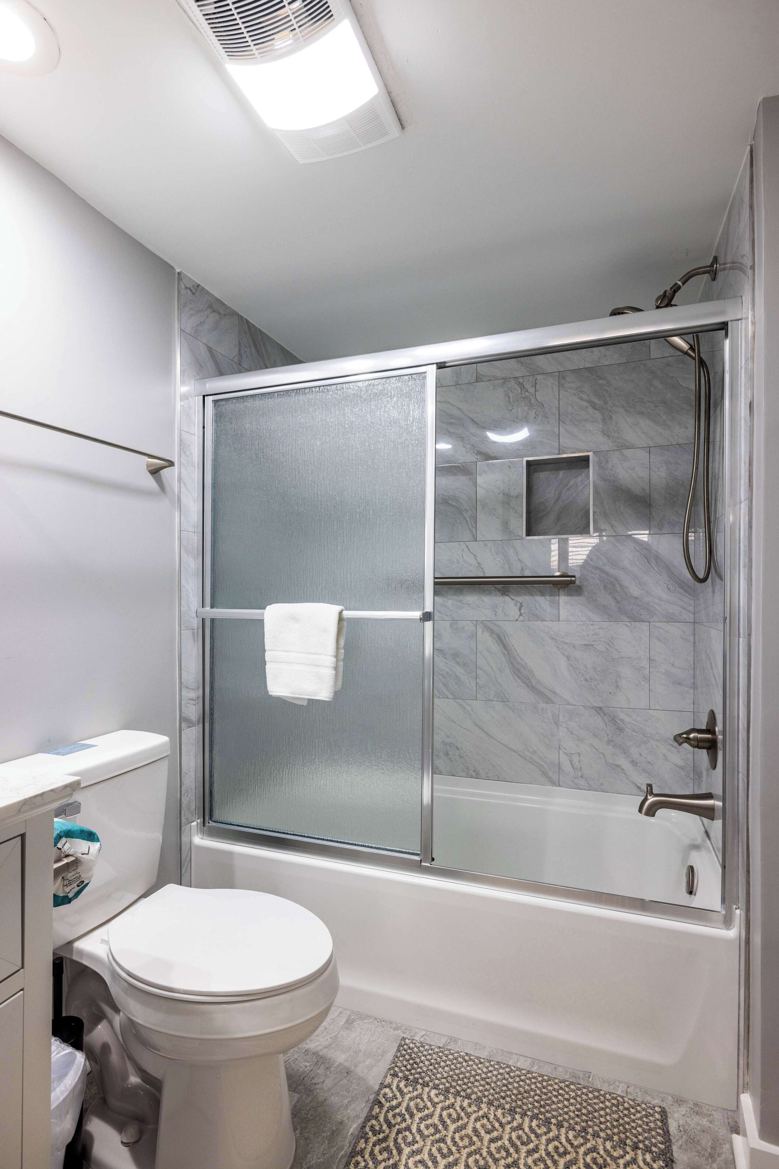 A modern bathroom with a glass-enclosed shower, a white toilet, and a marble-tiled shower area.