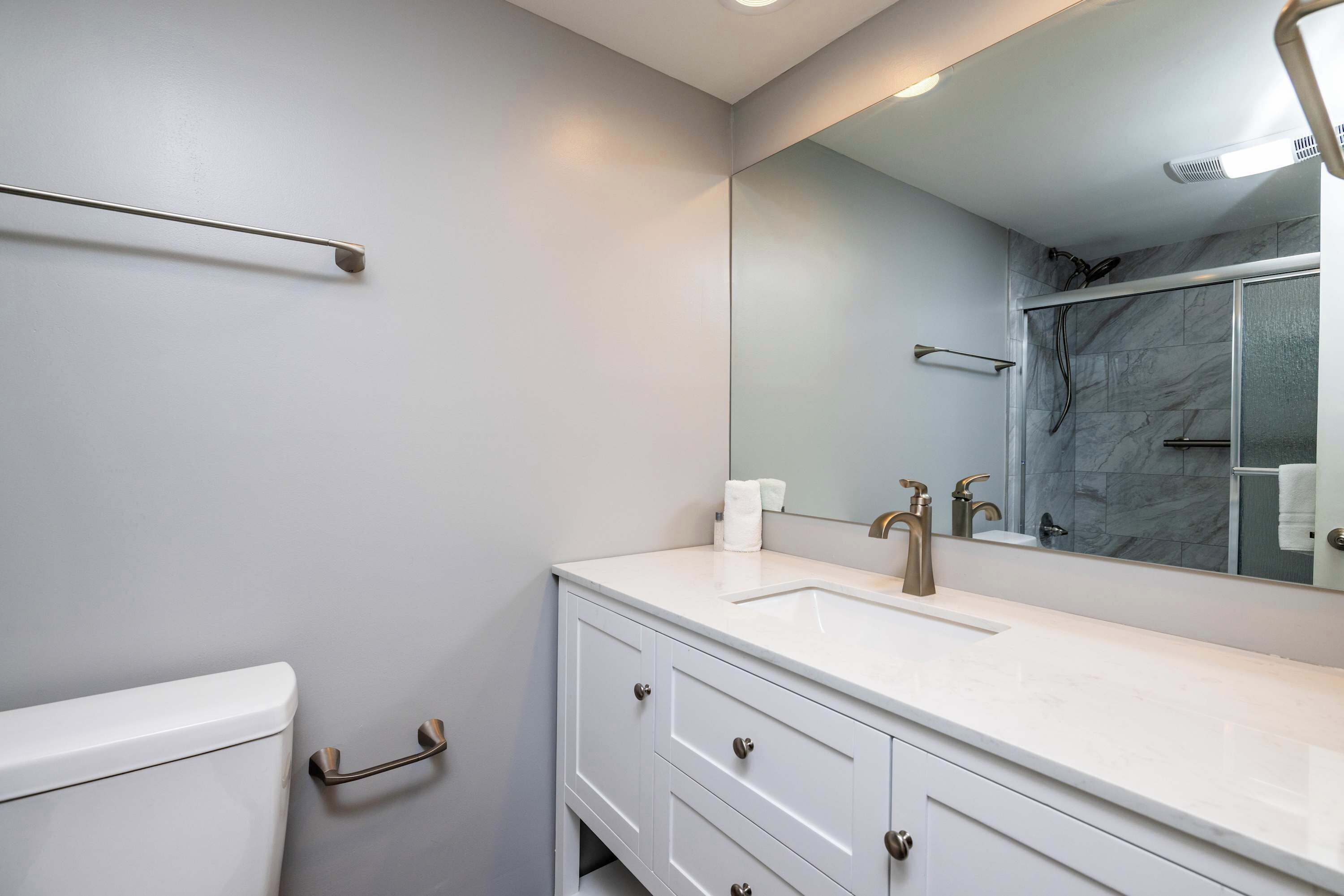 A bathroom with a toilet, sink, mirror, and shower.