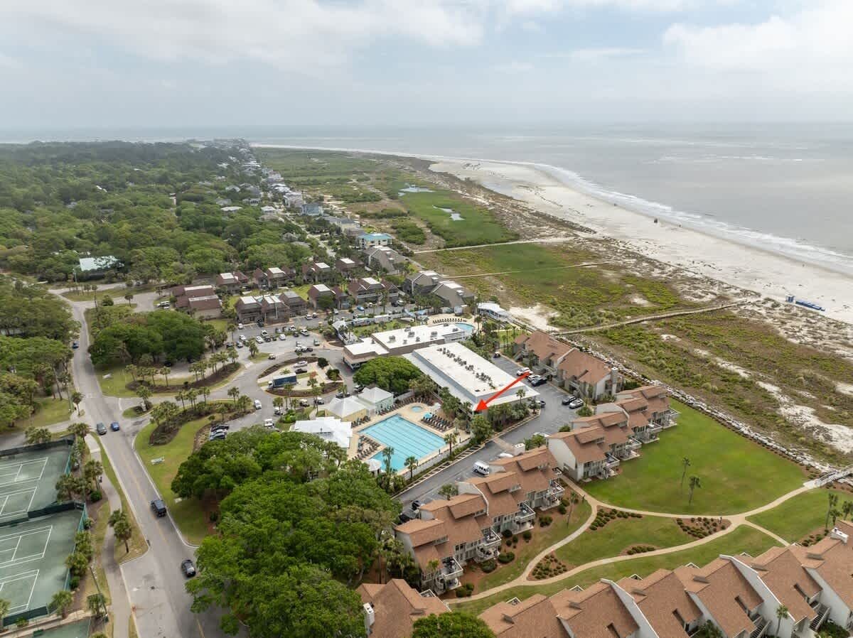 Luchtbeeld van een kustresort met een zwembad, tennisbanen en strandwoningen.