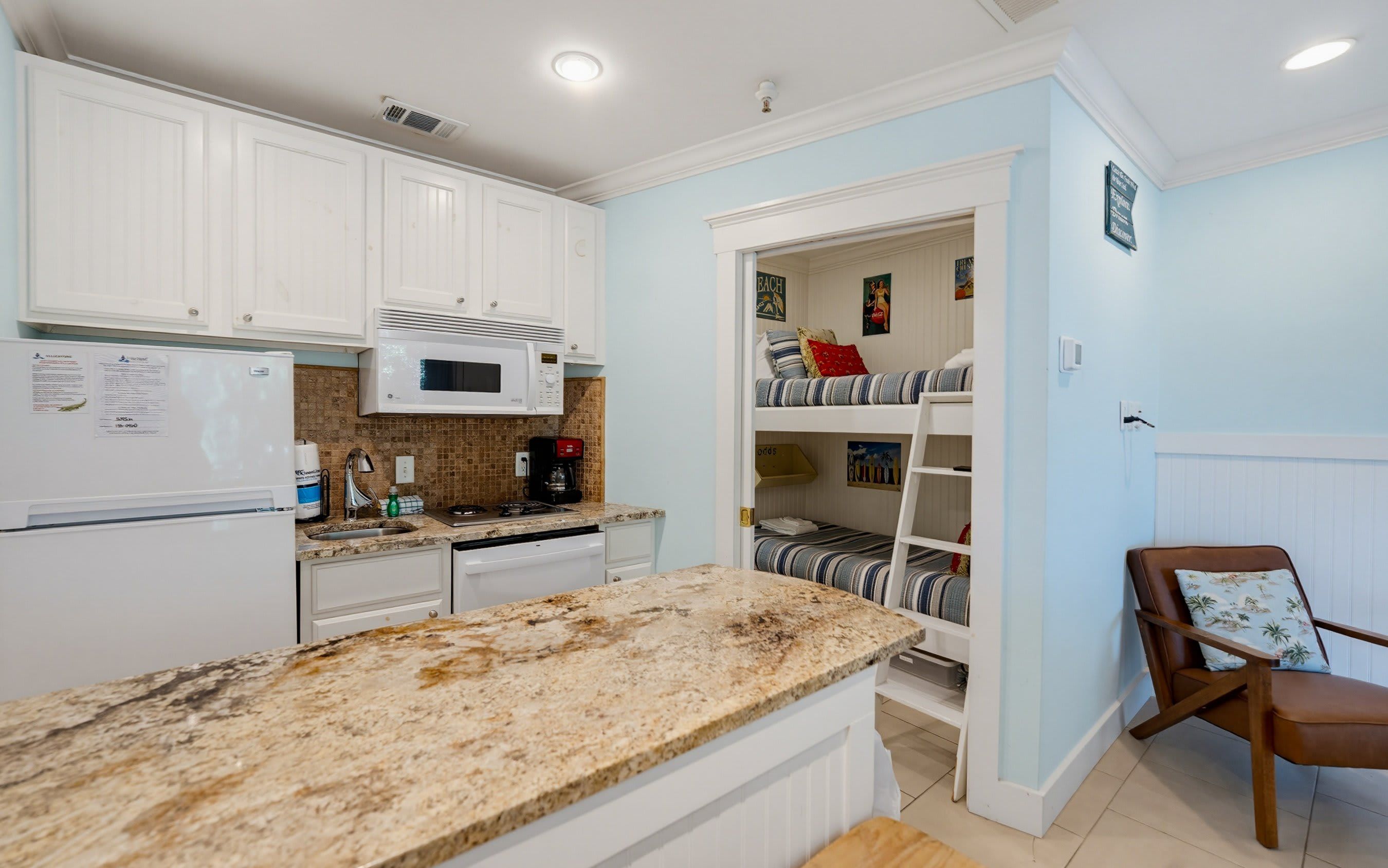 A kitchen with white cabinets, a microwave, a sink, and a granite countertop.