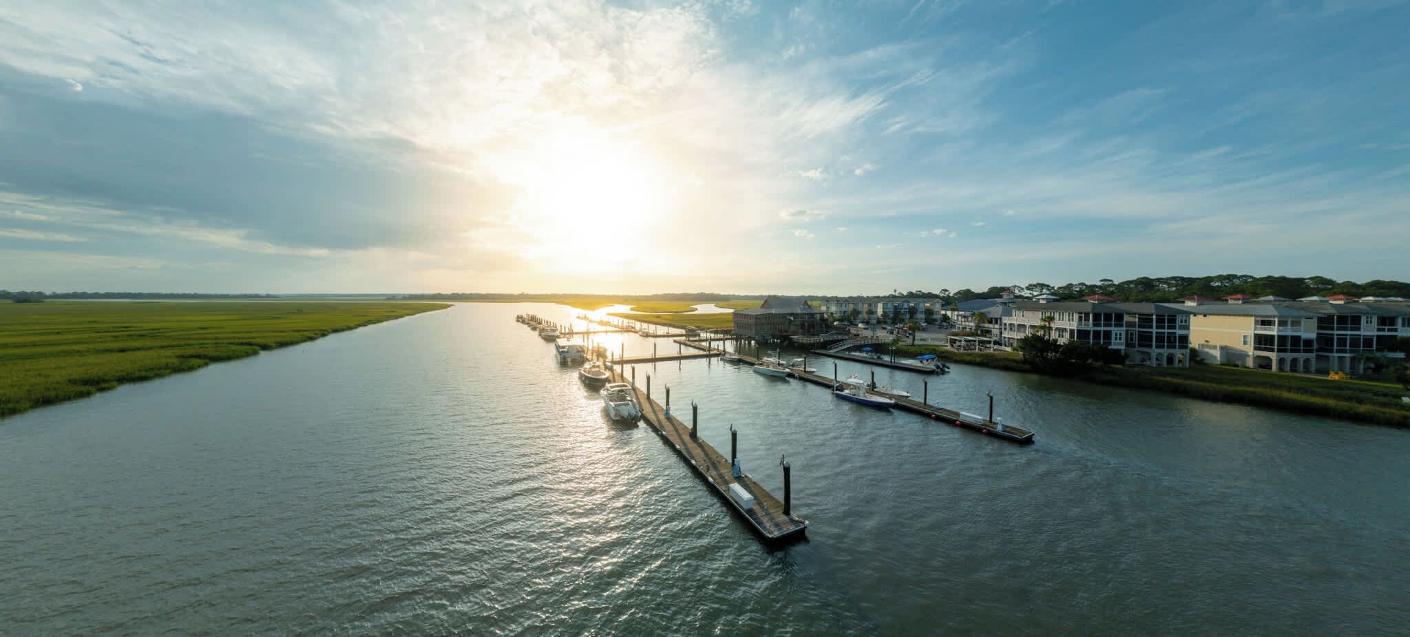 A riverfront marina with boats docked, a pier, and buildings along the riverbank.