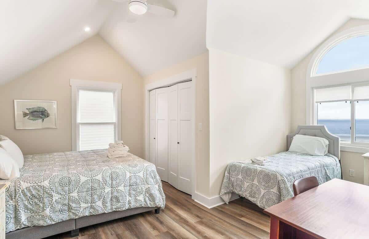 Un dormitorio con dos camas, un ventilador de techo, una ventana con vistas y una puerta.