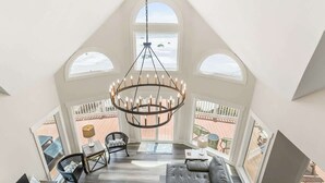 A high-ceilinged room with a chandelier, large windows, a sofa, and a dining table. - 805 Marlin Drive (Fripp Island)
