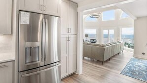 A modern kitchen with a stainless steel refrigerator, white cabinetry, and a view to a balcony with a sofa. - 805 Marlin Drive (Fripp Island)