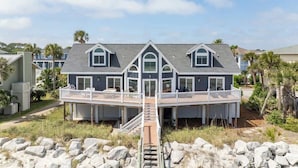 A two-story house with a balcony, a staircase leading to the deck, and a surrounding rocky landscape. - 805 Marlin Drive (Fripp Island)