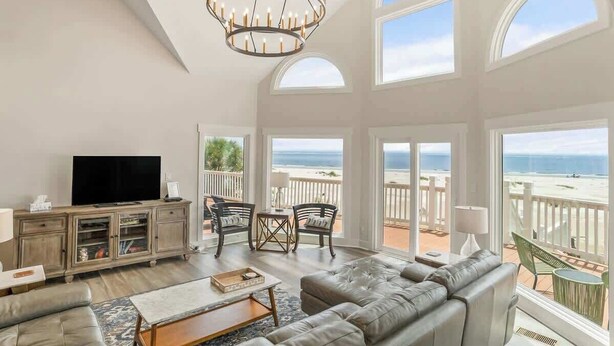 A spacious living room with a large TV, leather sofa, and a balcony with a view of the beach. - 805 Marlin Drive (Fripp Island)