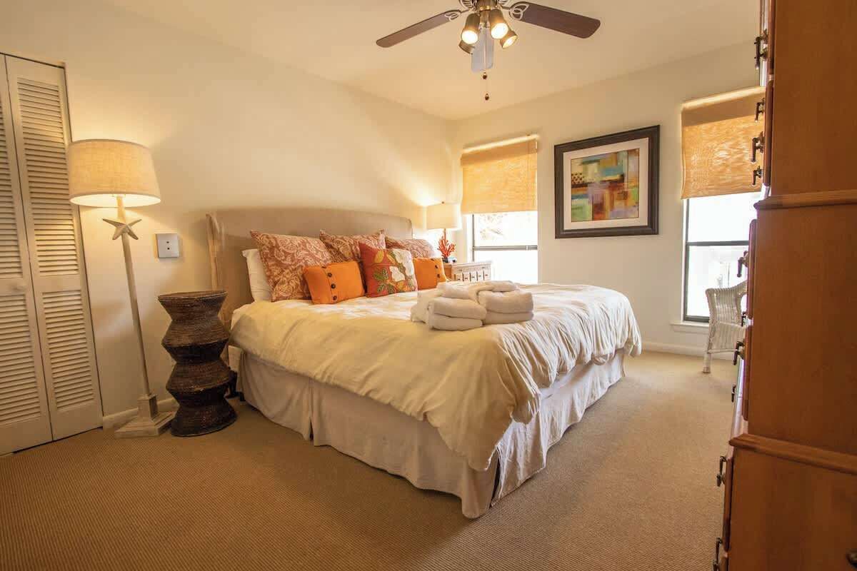 A bedroom with a bed, bedside lamps, a ceiling fan, and a window with blinds.