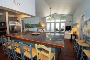 A spacious kitchen with a large island, bar stools, a dining area with a sofa, and a television.