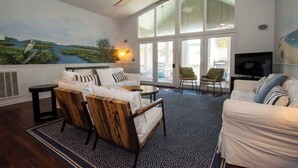 A living room with a large window, a ceiling fan, and a television. - 705 Silverside Road (Fripp Island)