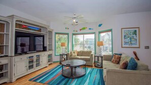 A living room with a TV, sofa, coffee table, and decorative fish on the wall. - 367 Ocean Point Drive - Pelican Point (Fripp Island)