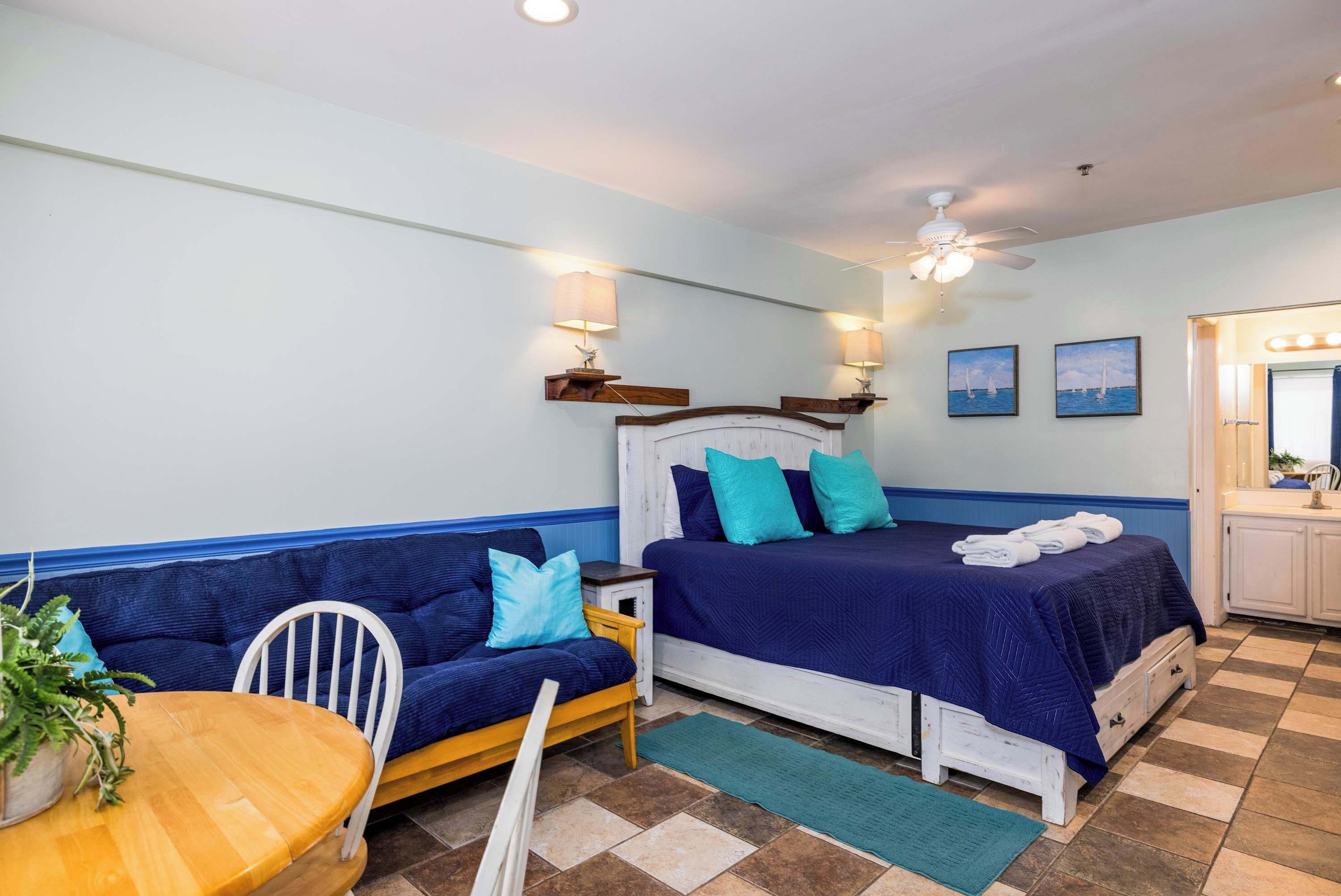 Una habitación con cama, sofá, una mesita y ventilador de techo.
