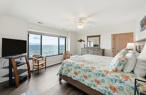 Un dormitorio con cama, escritorio, silla, televisor y vista al mar.