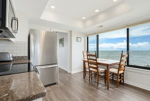 Una cocina moderna con un refrigerador de acero inoxidable, una mesa de comedor con sillas y vistas al océano a través de grandes ventanales.