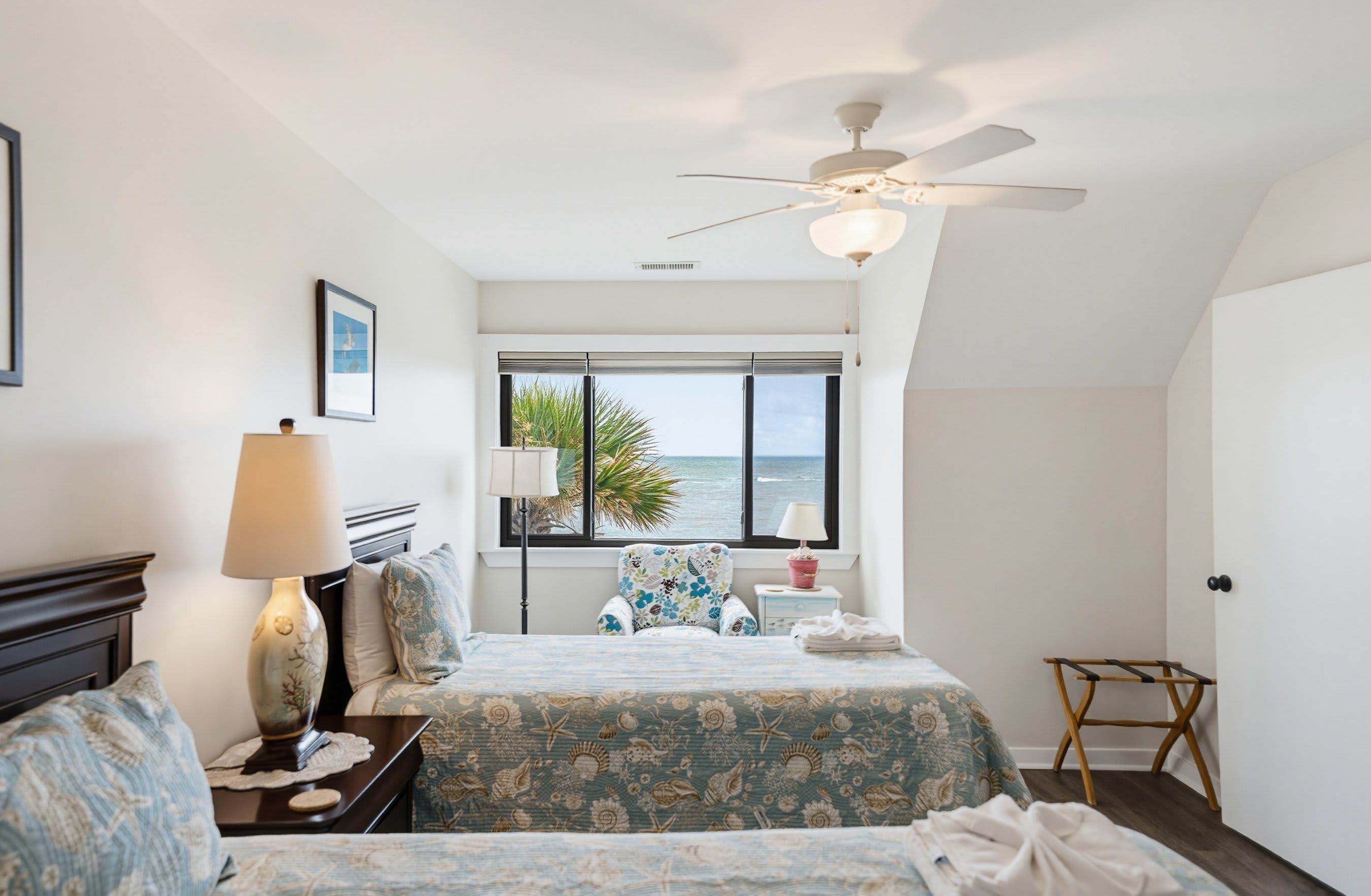 A bedroom with a bed, bedside tables, a lamp, a chair, a window with a view, and a ceiling fan.