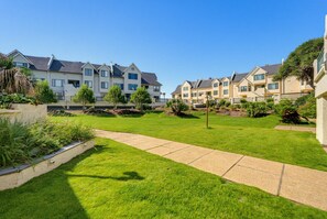 Een wooncomplex met meerdere tweelaagse huizen, een verzorgd gazon en een verhard pad.