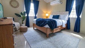 Un dormitorio con una cama de madera, una lámpara de noche, una planta en maceta y un espejo redondo en la pared.