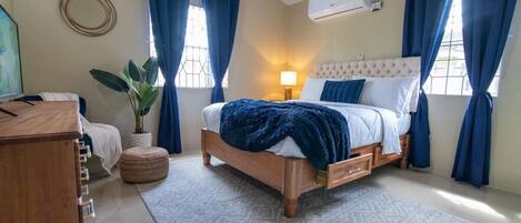 A bedroom with a wooden bed, a bedside lamp, a potted plant, and a round mirror on the wall.