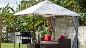 Un patio con zona de estar techada, una parrilla y una mesa de comedor.