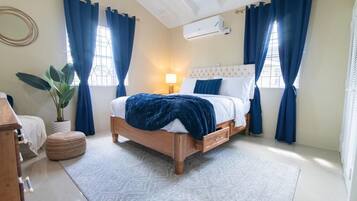 A bedroom with a wooden bed, blue curtains, a potted plant, and a white air conditioning unit on the wall.
