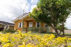 A yellow house with a green porch and a tree in the front yard. - Stafford Oasis (Ocho Rios)