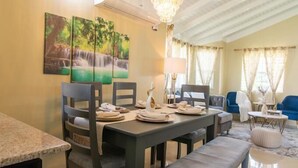 Un comedor con una mesa dispuesta para cuatro, una araña y un cuadro de una cascada en la pared.