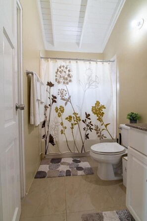 A bathroom with a shower curtain featuring floral designs, a toilet, and a small potted plant on the counter. - Stafford Oasis (Ocho Rios)