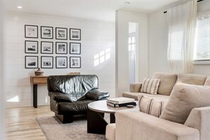 Un salon moderne avec un fauteuil en cuir, un canapé beige, une table basse et un mur décoré de tableaux encadrés.