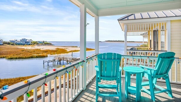 Une véranda couverte avec des chaises turquoise et une vue sur l’eau et les maisons.