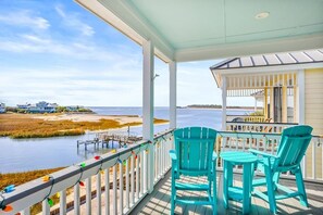 Une véranda couverte avec des chaises turquoise et une vue sur l’eau et les maisons.