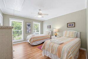 A bedroom with two beds, a ceiling fan, and large windows with blinds.