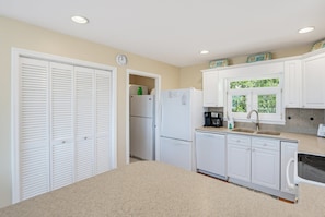 Cocina compacta con armarios blancos, refrigerador, lavavajillas y ventana con vista a zonas verdes.