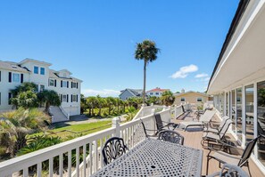 A balcony with outdoor furniture, a white railing, and a view of a residential area with houses and palm trees.