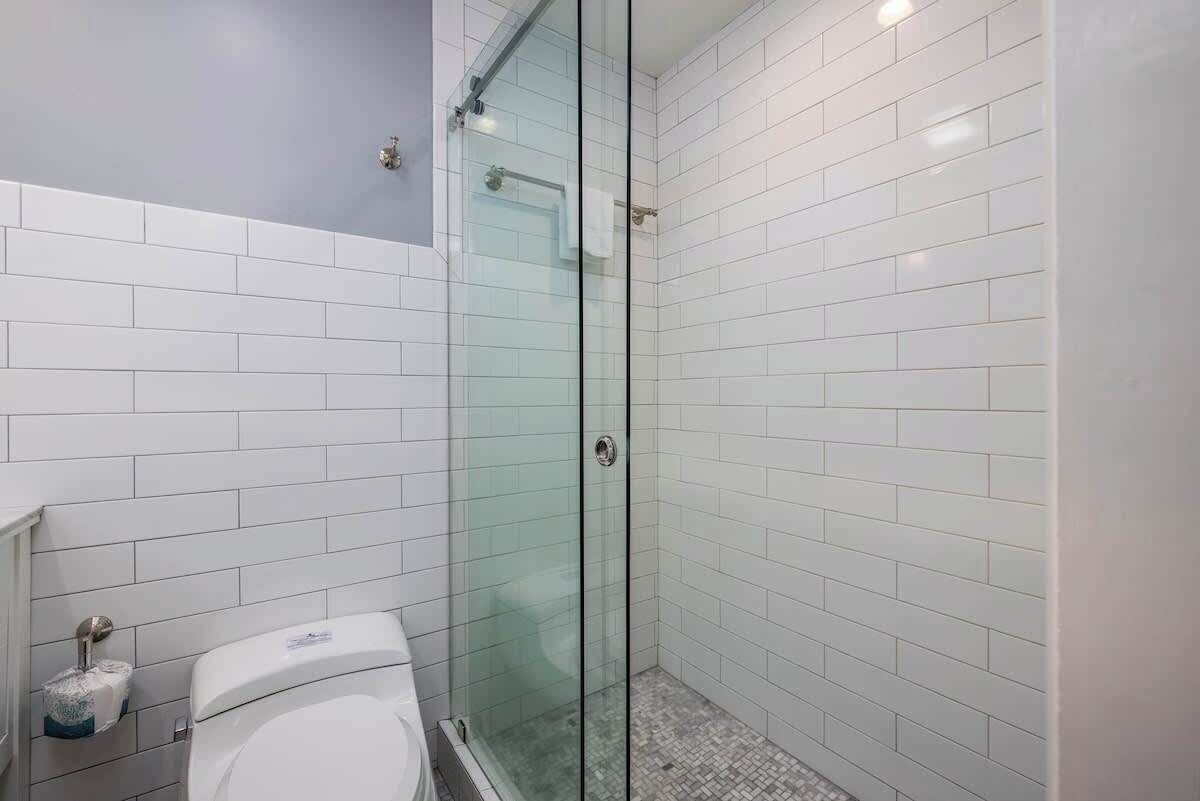 A bathroom with white tiled walls, a glass shower enclosure, and a toilet.