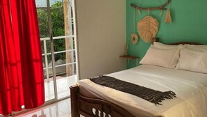 A bedroom with a bed, a window with red curtains, a green wall, and a view of greenery outside. - Casa Guiwa Hostel (Dibulla)