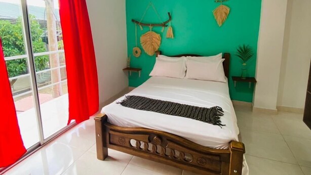 A bedroom with a bed, a red curtain, a green wall, and a view through a glass door. - Casa Guiwa Hostel (Dibulla)