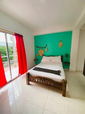 A bedroom with a bed, a window with red curtains, a green wall, and a view of greenery outside. - Casa Guiwa Hostel (Dibulla)