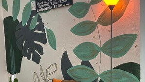 A room with a check-in sign, a brown sofa with an orange pillow, a potted plant, and a floor lamp. - Casa Guiwa Hostel (Dibulla)
