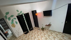 A living room with a sofa, a floor lamp, and a TV mounted on the wall. - Casa Guiwa Hostel (Dibulla)
