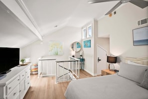 Quarto moderno com uma cama grande, televisão, escrivaninha e escada para um andar superior.