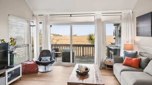 Un salon spacieux doté d’une grande porte-fenêtre coulissante donnant sur une terrasse, d’un téléviseur à écran plat, d’un canapé confortable et d’une table basse.