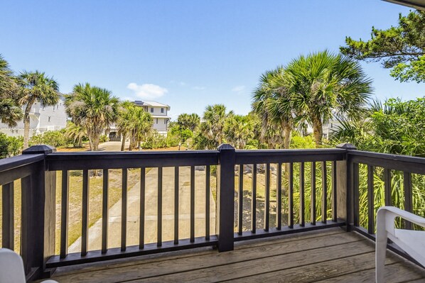 A wooden deck with a railing, overlooking a residential area with palm trees and houses.