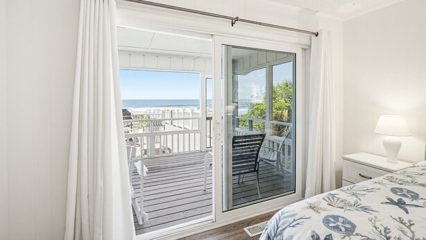 Een slaapkamer met balkon, een bed met bloemenbeddengoed, een nachtkastje met lamp en uitzicht op zee.