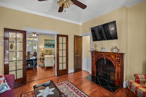 A spacious living room with hardwood flooring, a fireplace, a television mounted on the wall, and a cozy seating area with a patterned rug.