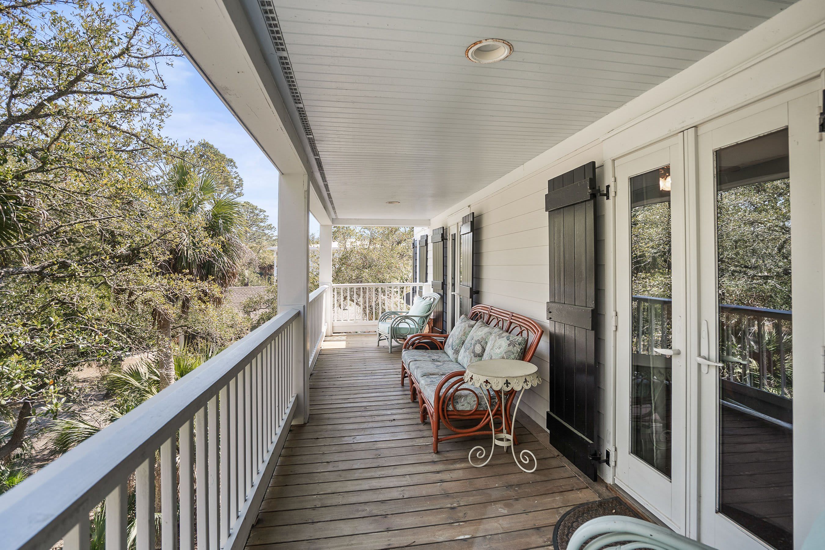 A covered porch with a wooden floor, a white railing, and a seating area with a wicker sofa and a small table.
