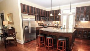 A kitchen with wooden cabinets, a stainless steel refrigerator, a granite countertop, and three bar stools. - 813 Bonito Road (Fripp Island)