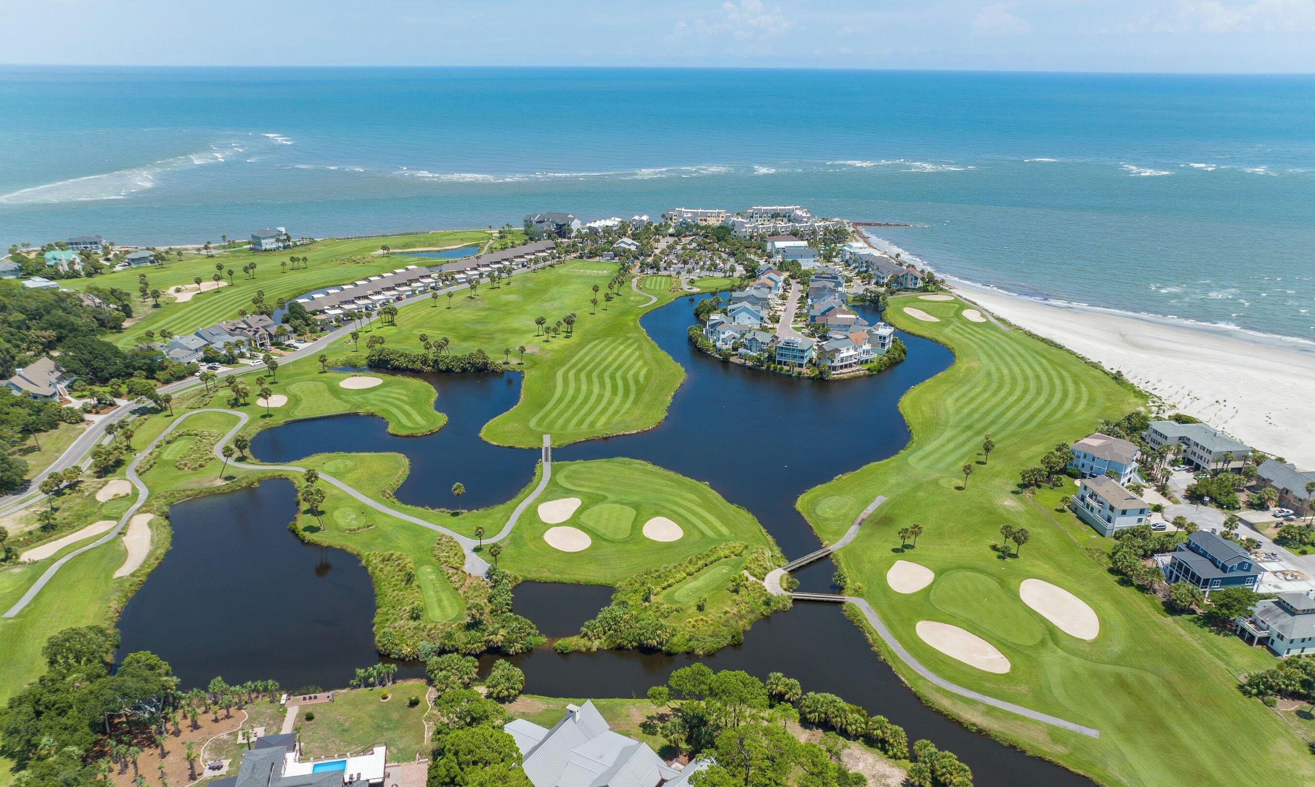 Een kustgolfbaan met waterhindernissen, een strand en woonhuizen.