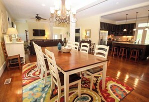 A dining area with a wooden table and white chairs, a chandelier, and a colorful rug. - 813 Bonito Road (Fripp Island)