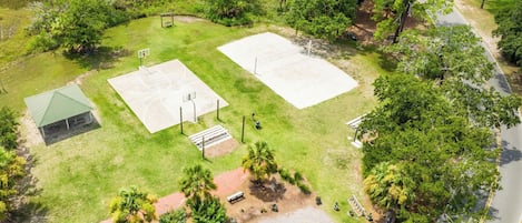 Ovenudblik over en ejendom med basketballbane, en lille pavillon og parkeringsplads.